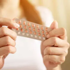 Dłonie trzymające opakowanie tabletek antykoncepcyjnych.