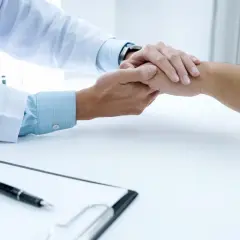 Lekarz trzyma pacjenta za rękę, okazując wsparcie. Dymista cena usług medycznych nie powinna być barierą w otrzymaniu pomocy.
