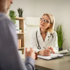 Lekarka z receptą w dłoni, słuchając pacjenta, pokazuje, ile ważne jest skierowanie do specjalisty.