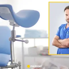 Ginekolog w niebieskim kitlu, z maską w kieszeni, obok fotela ginekologicznego. To miejsce, gdzie kobiety dbają o swoje zdrowie w każdym okresie życia.