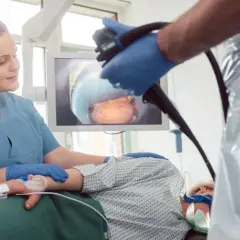 Lekarz wykonuje kolonoskopię, a pielęgniarka asystuje. Na ekranie widok wnętrza jelita. Sprawdź, jaka jest kolonoskopia cena.