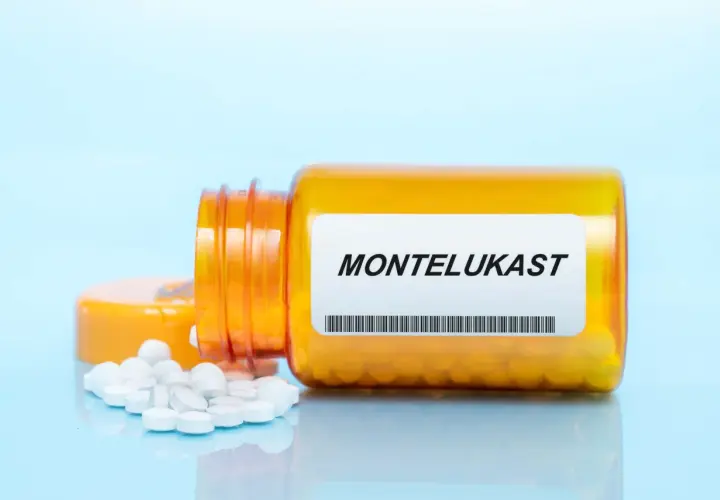 Pomarańczowa buteleczka z lekami, na której widnieje napis MONTELUKAST. Obok rozsypane białe tabletki.