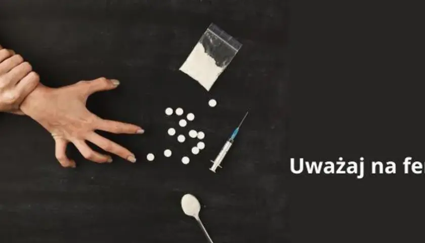 Dwie dłonie walczą o kontrolę nad przedmiotami związanymi z narkotykami, w tym proszkiem, tabletkami i strzykawką. Uważaj na fentanyl.