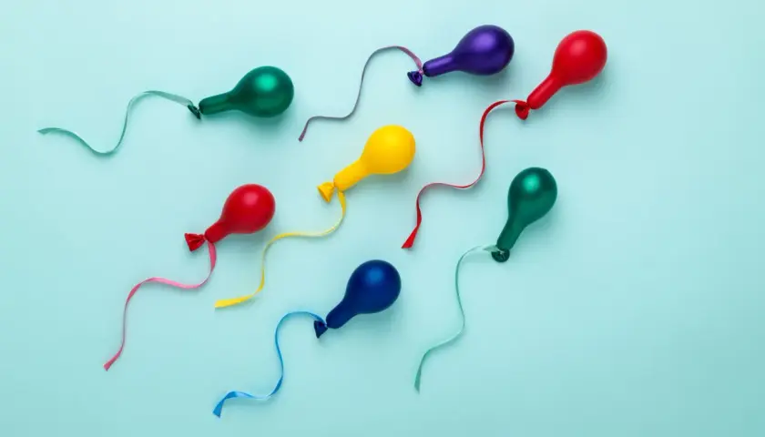 Kolorowe balony w kształcie plemników, symbolizujące kobiecy wytrysk, unoszą się na błękitnym tle.