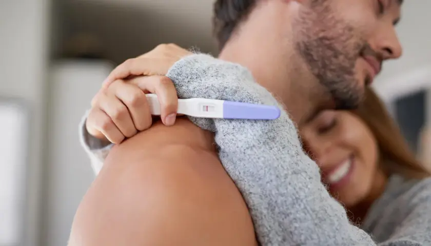 Para z uśmiechem przytula się, trzymając test ciążowy z dwoma kreskami. Po długiej drodze, być może przez invitro, marzenie o dziecku staje się rzeczywistością.