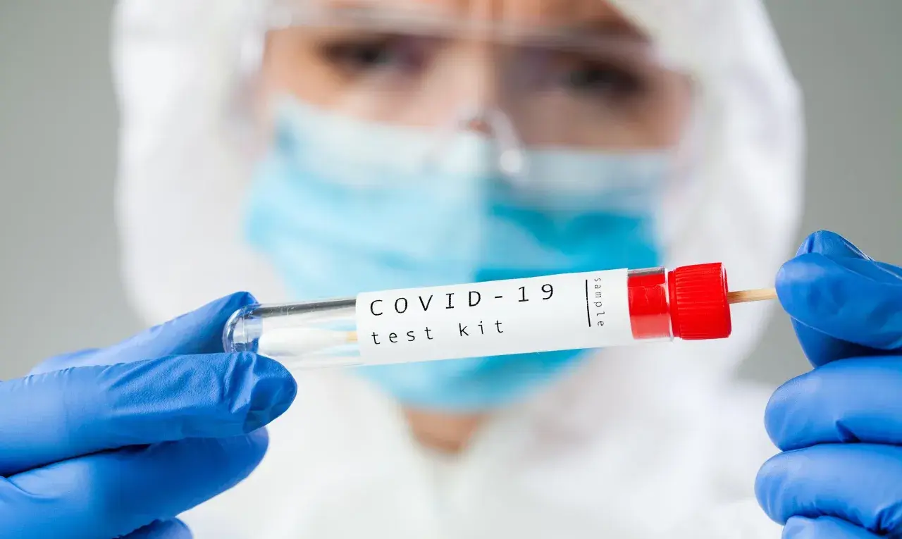 Osoba w kombinezonie ochronnym trzyma probówkę z wymazem. Zastanawiasz się, ile kosztuje test na COVID-19?